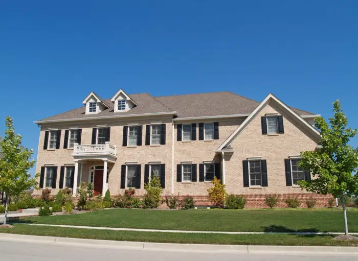 A large brick colonial home with twin dormers, a columned portico, and mature landscaping