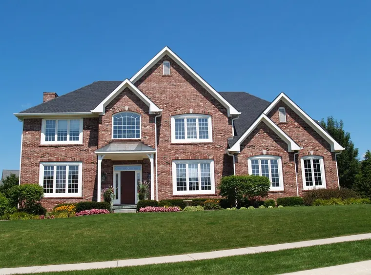 A red-brick two-story home with white trim and flowering beds